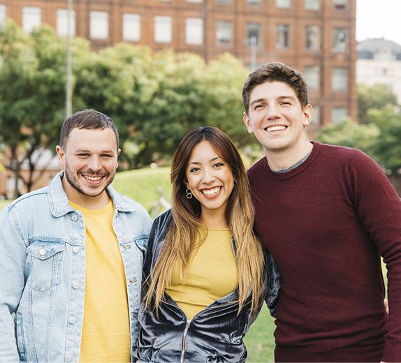 Three students, two men and one woman, smiling on the schoolyard