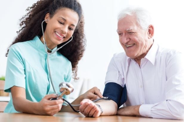 CNA helps older man check blood pressure at a medical facility.