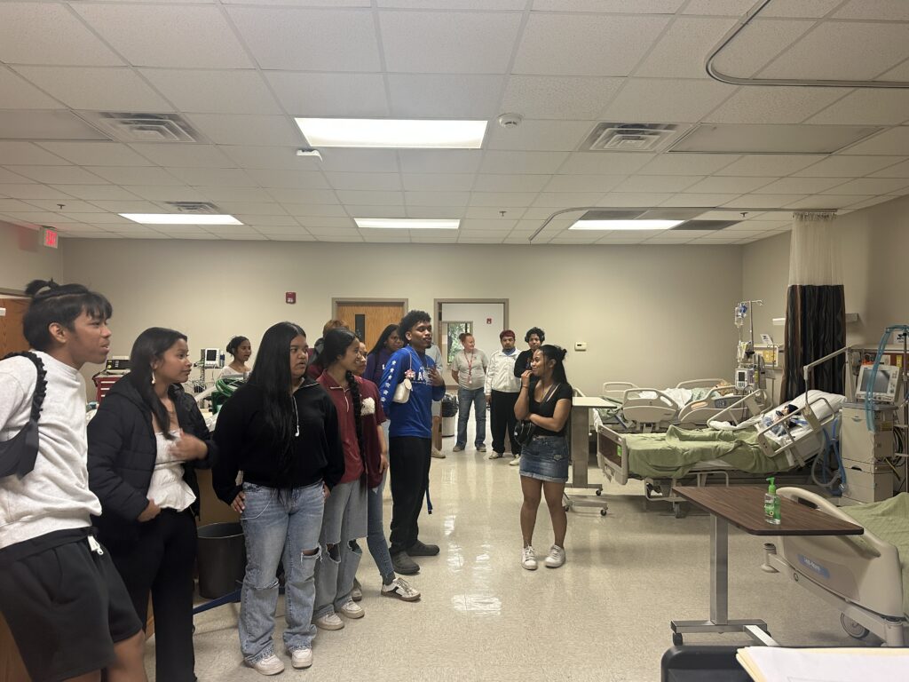 Prospective Marshallese students visit BRTC's nursing simulation lab, observing a hospital bed with a patient mannequin and medical equipment during a campus Preview Day tour.