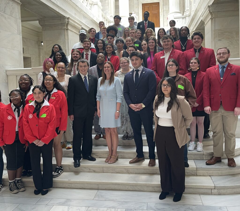 Students from across Arkansas community colleges, many wearing red blazers, pose on a marble staircase with Arkansas Governor Sarah Sanders during the ACC Student Leadership Academy.