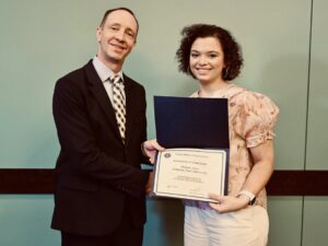 A young woman receives an FBI Certificate of Completion from a suited official, recognizing her successful completion of the FBI Collegiate Academy, representing Arkansas State University.