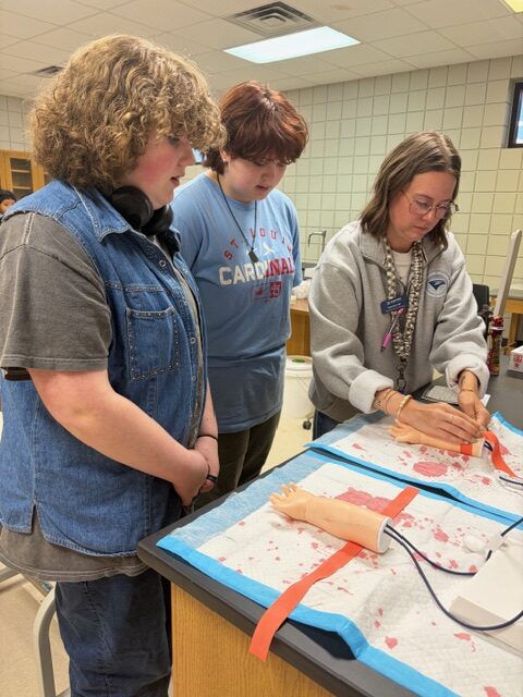 Pocahontas 8th grade students watch as phlebotomy instructor shows them how to draw blood.