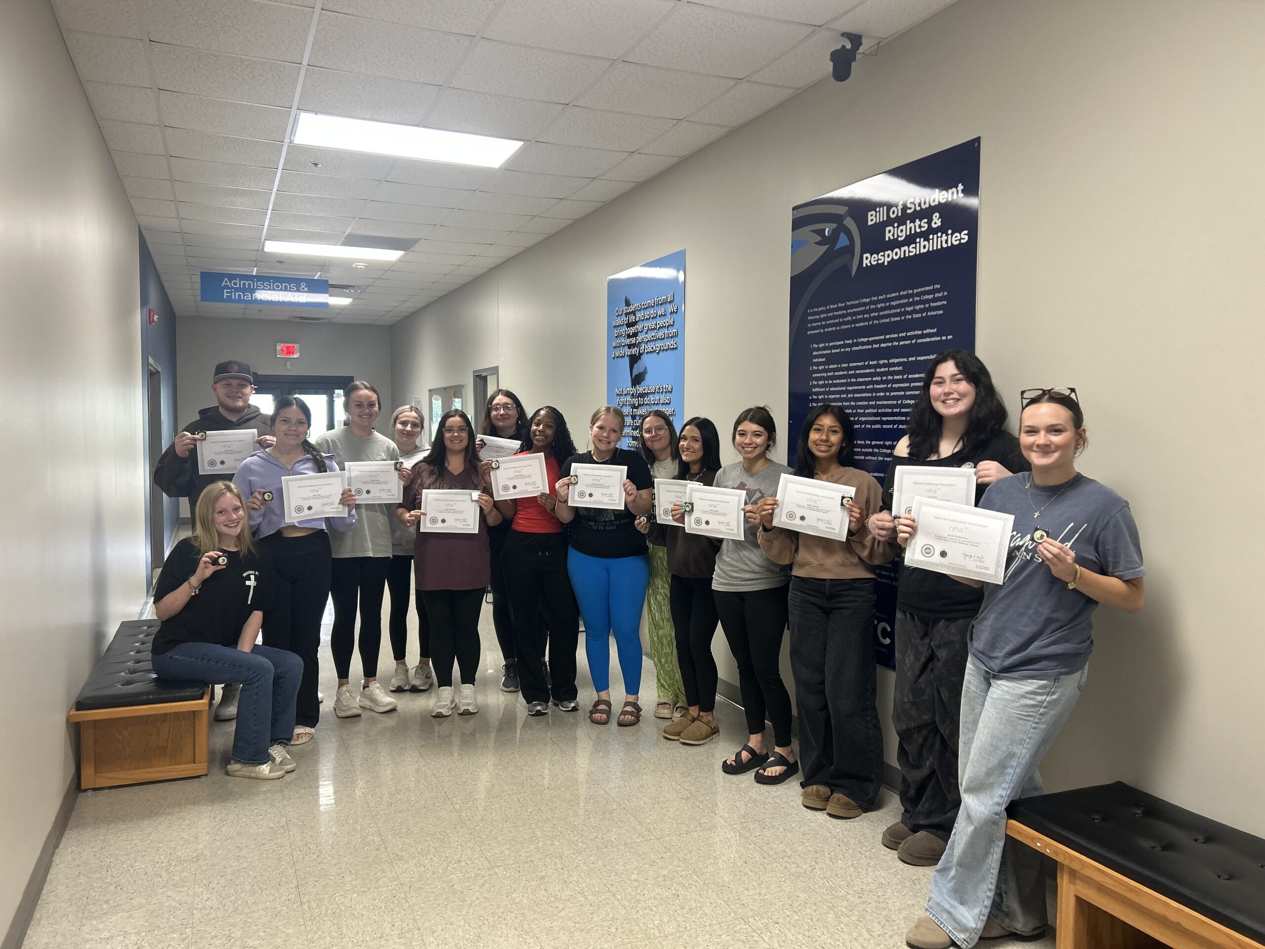 A group of students stand in a hallway, each holding a certificate and a small pin.