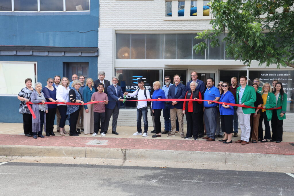 A group of community leaders and representatives hold a long red ribbon for a ceremonial cutting in front of the Black River Technical College Adult Education building in downtown Paragould.