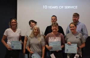Six individuals stand together in front of a projection screen that reads "10 YEARS OF SERVICE".