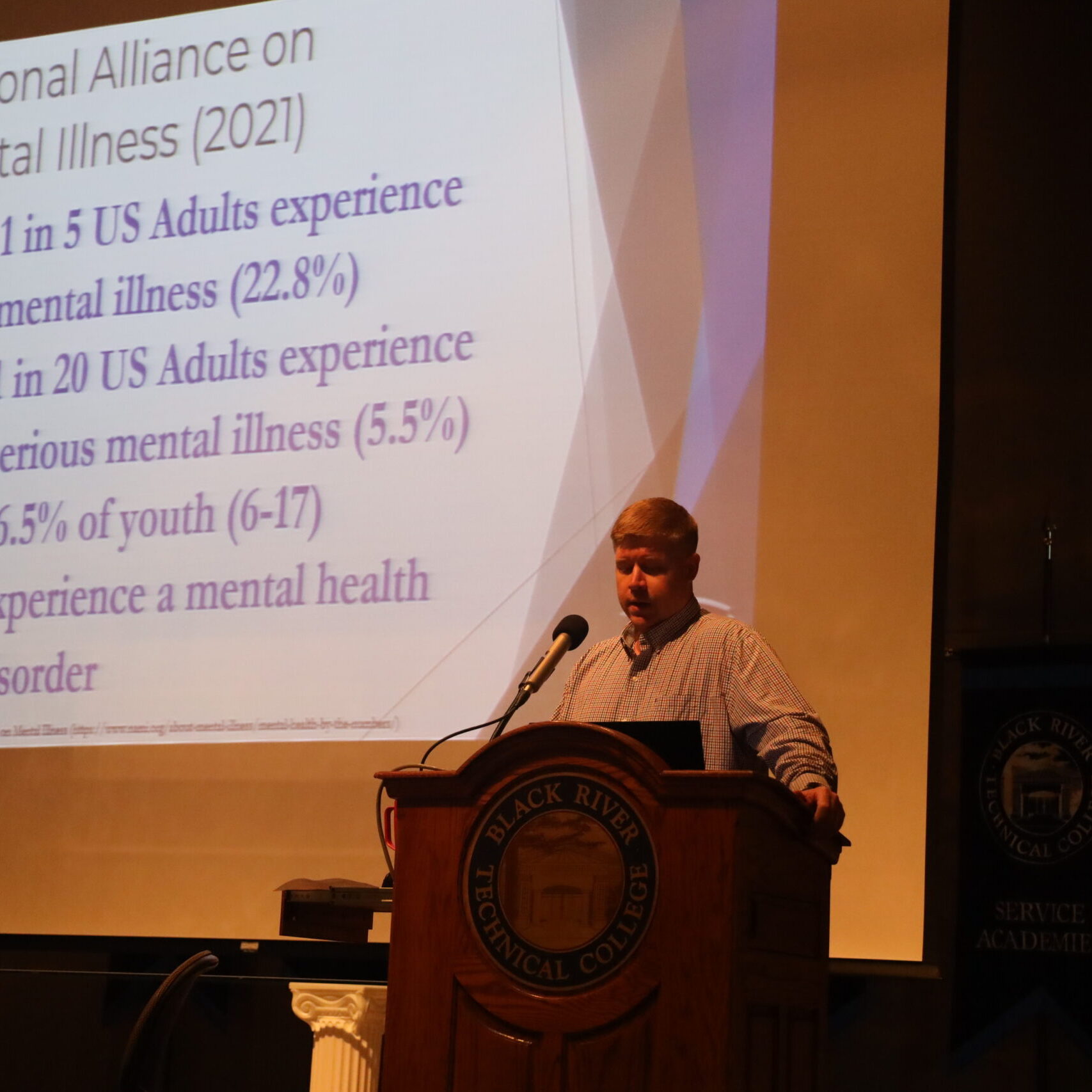Man standing at a podium with a slideshow behind him.