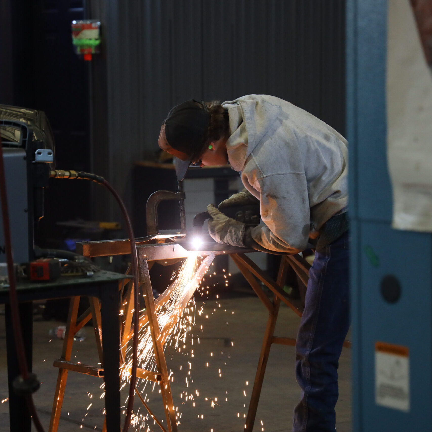A student welder in protective gear works on a metal piece, producing a bright arc and cascade of sparks during BRTC's annual ARC welding competition.