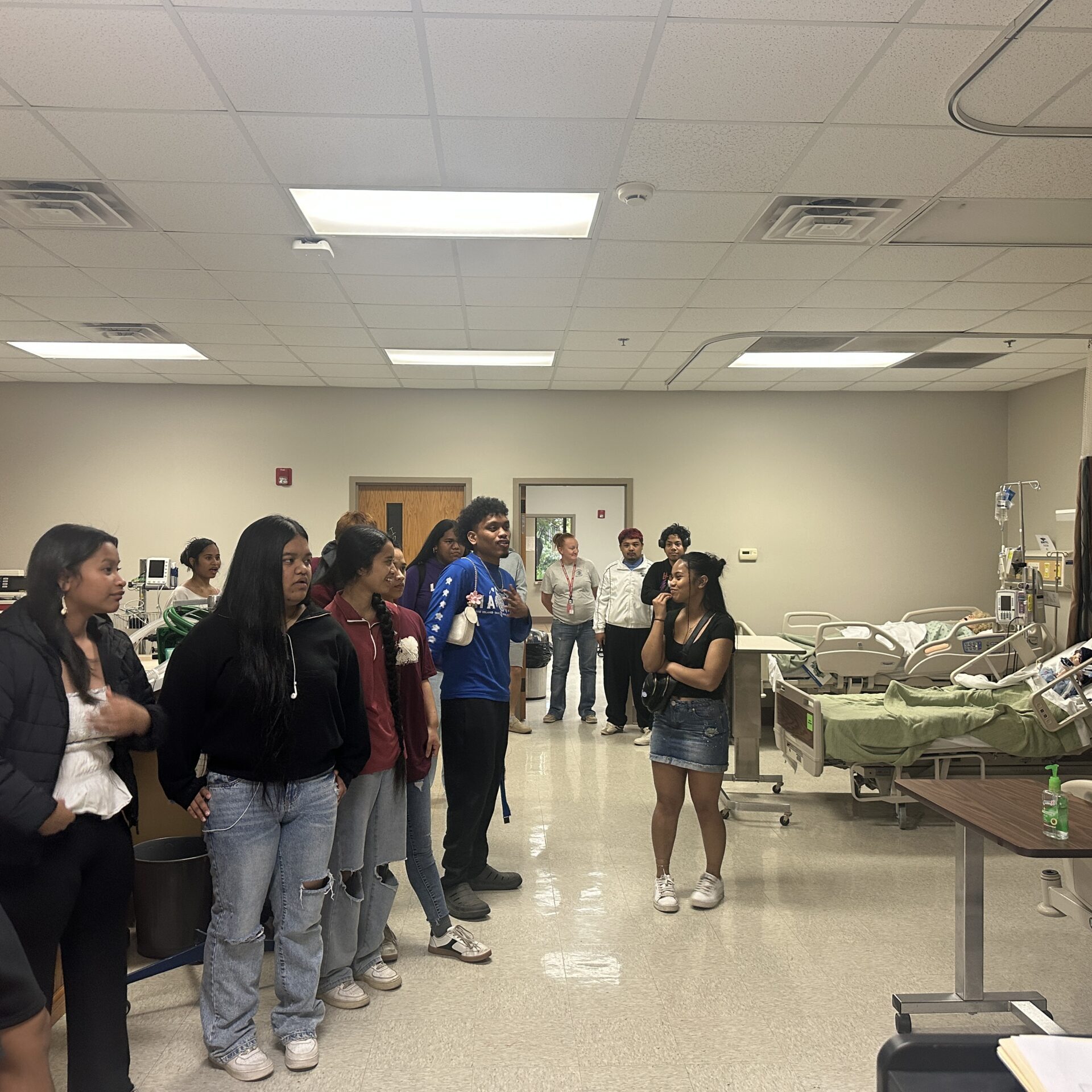 Prospective Marshallese students visit BRTC's nursing simulation lab, observing a hospital bed with a patient mannequin and medical equipment during a campus Preview Day tour.
