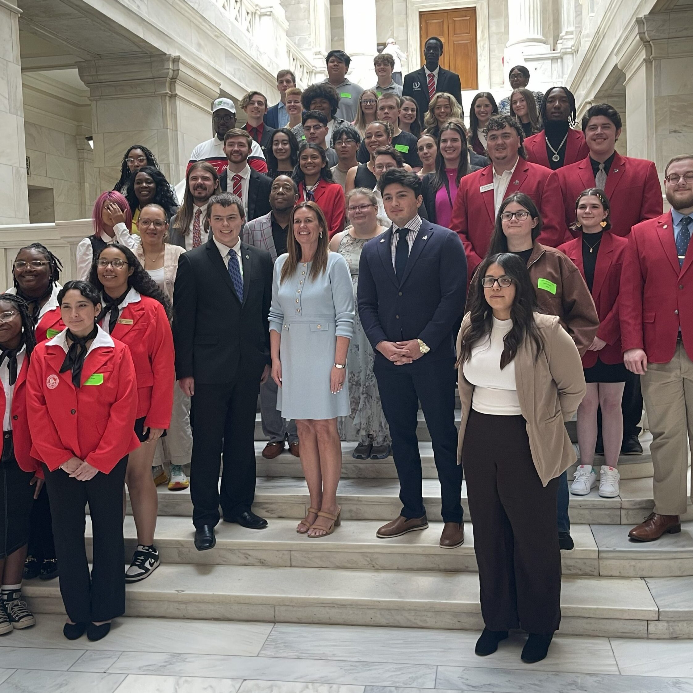 Students from across Arkansas community colleges, many wearing red blazers, pose on a marble staircase with Arkansas Governor Sarah Sanders during the ACC Student Leadership Academy.