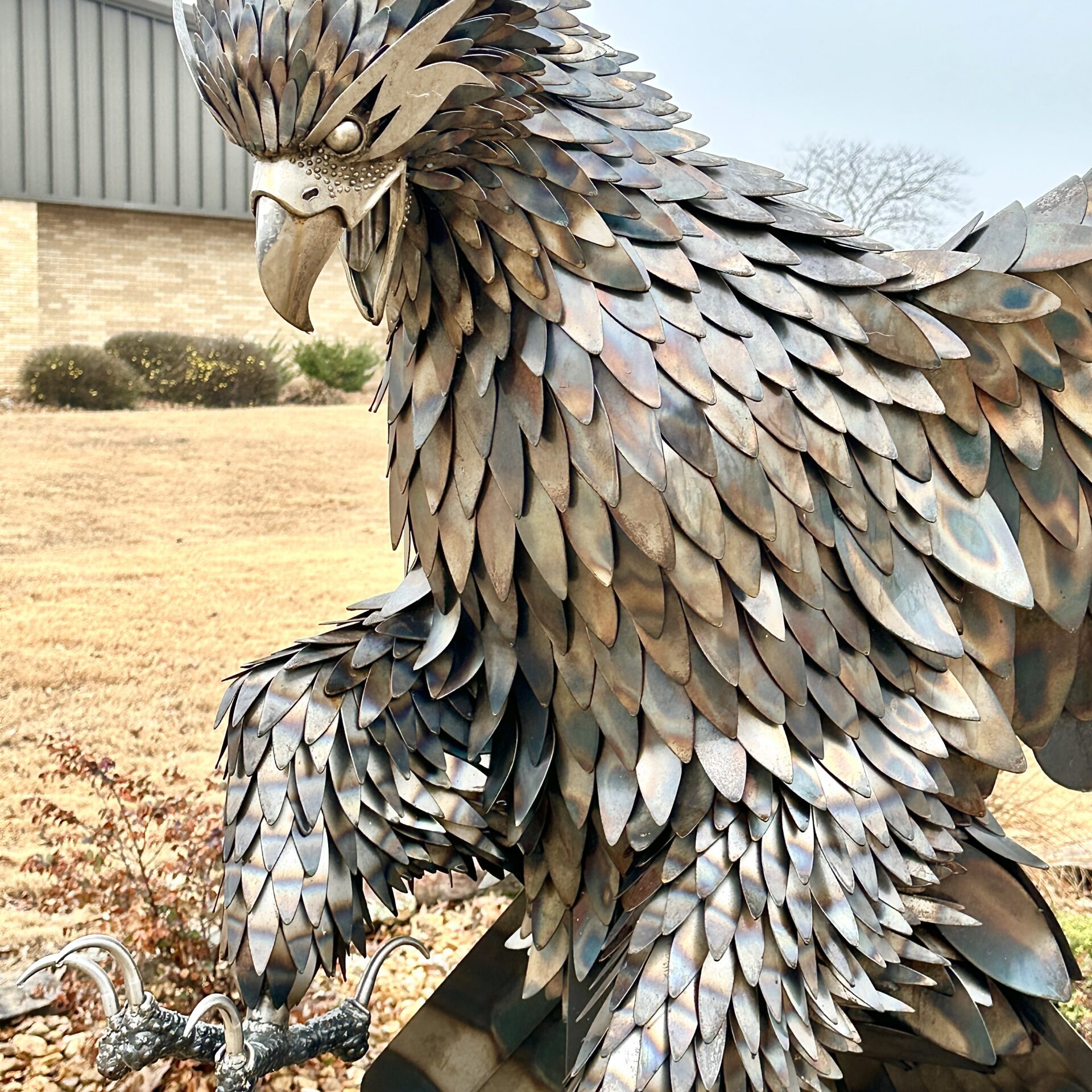 A close-up, side-profile view of a large eagle sculpture crafted entirely from welded, overlapping metal plates that resemble feathers.